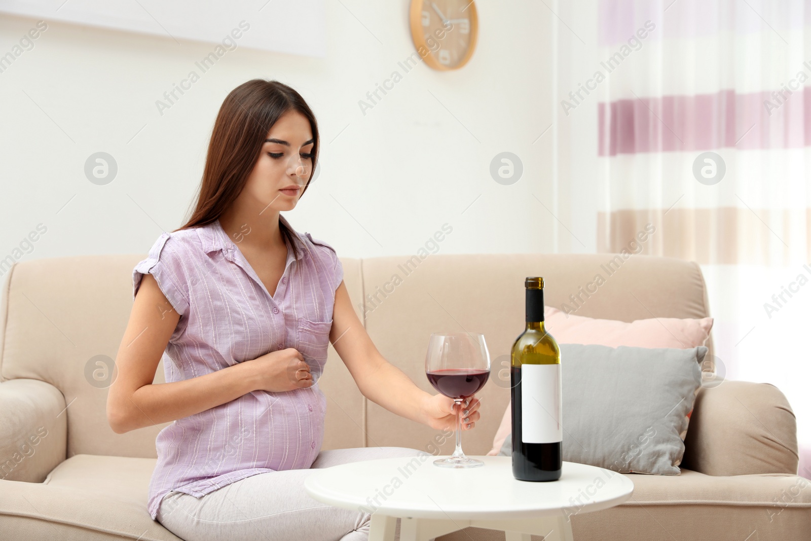 Photo of Future mother with glass and bottle of wine indoors. Alcohol abuse during pregnancy