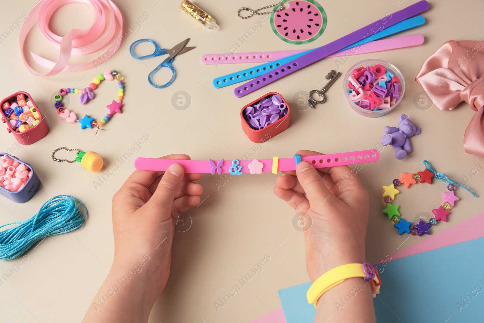 Photo of Child making beaded jewelry and different supplies on beige background, above view. Handmade accessories