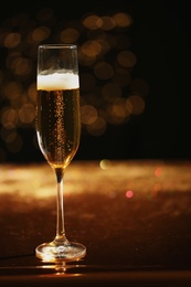 Photo of Glass of champagne with golden bubbles on table against blurred background. Space for text