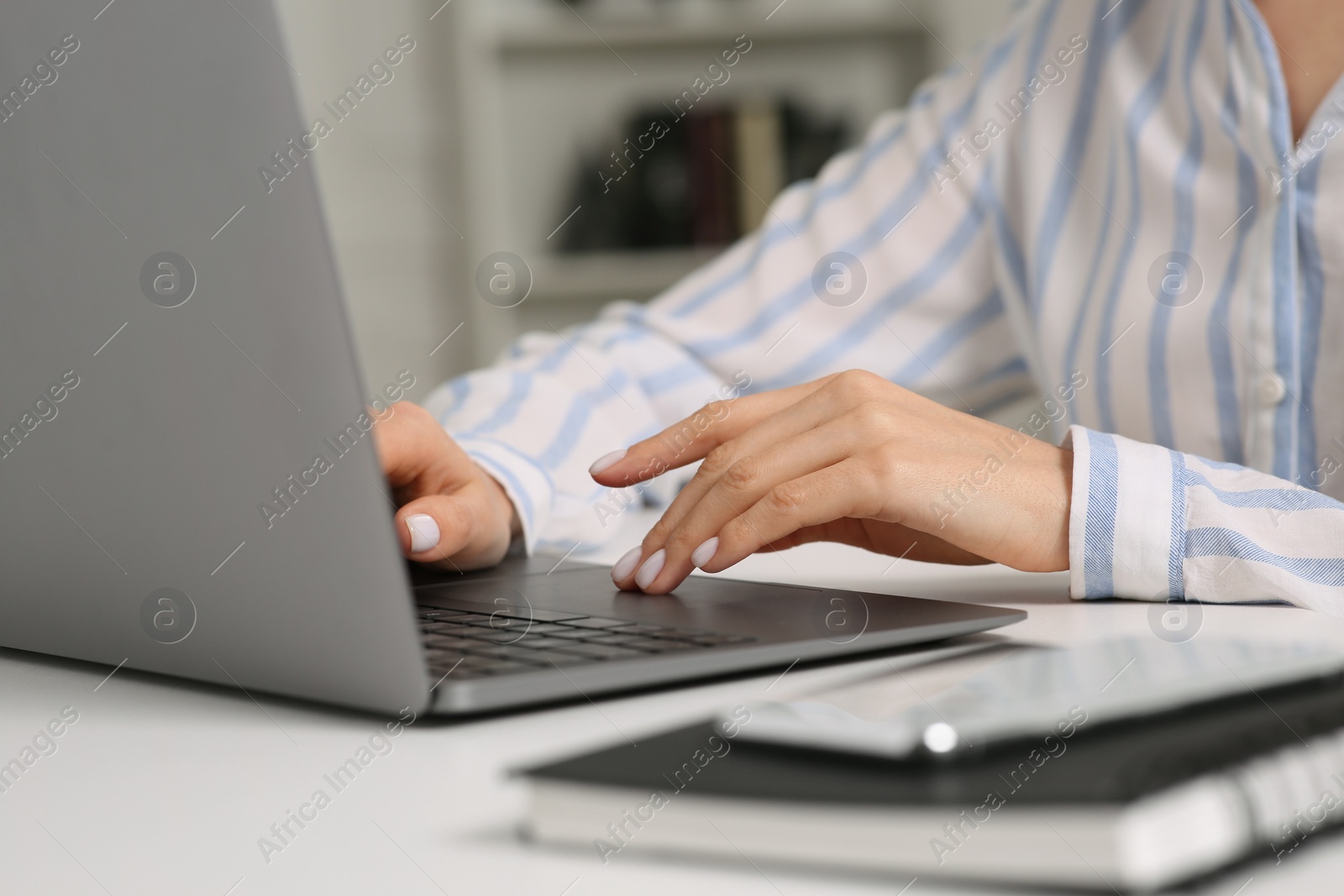 Photo of Woman working with laptop at white desk indoors, closeup