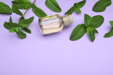 Photo of Bottle of essential oil and mint on violet background, above view. Space for text