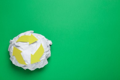 Photo of Crumpled paper with recycling symbol on green background, top view. Space for text