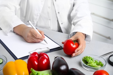 Scientist with clipboard and fresh tomato at table in laboratory, closeup. Poison detection