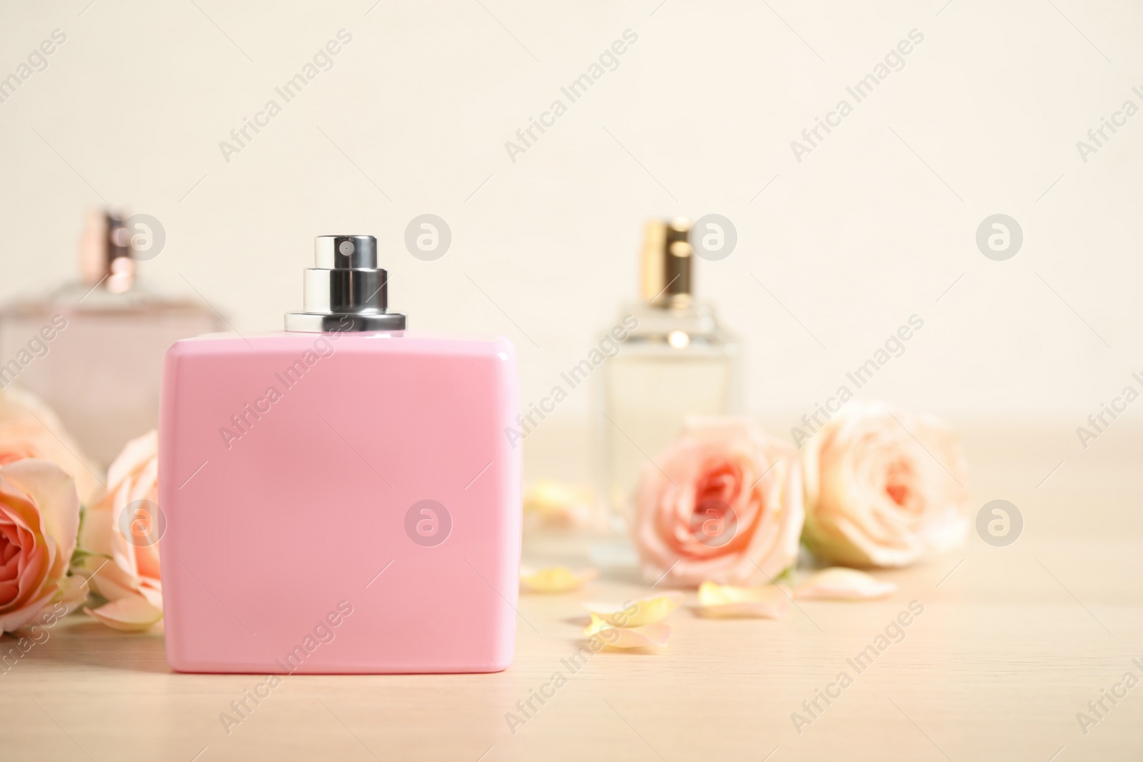 Photo of Bottles of perfume and beautiful flowers on wooden table. Space for text
