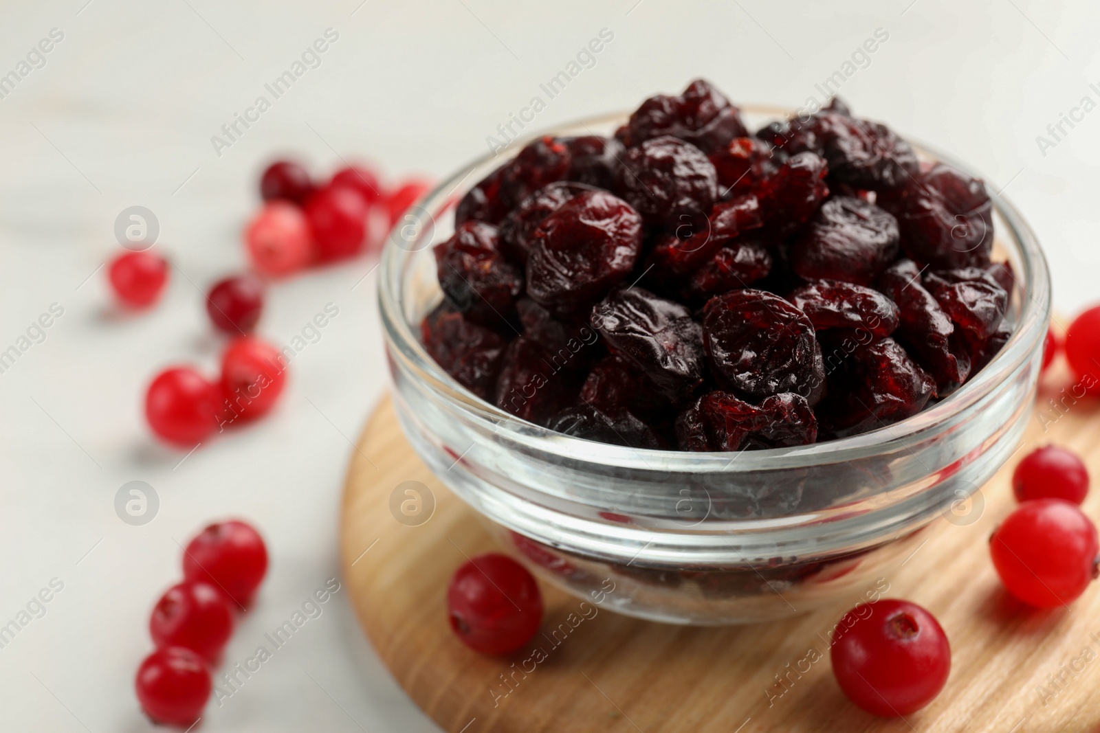 Photo of Tasty dried cranberries in bowl and fresh ones on white table, closeup. Space for text