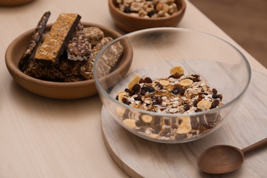 Photo of Glass bowl with cereal and grains on wooden table. Healthy granola bar preparation