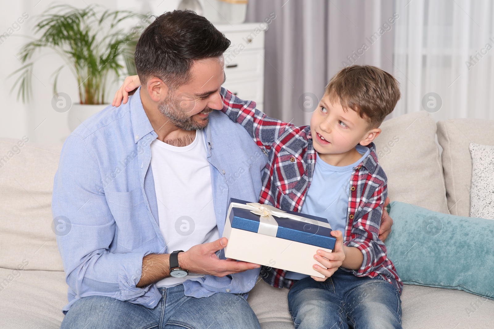 Photo of Cute little boy presenting his father with gift on sofa at home