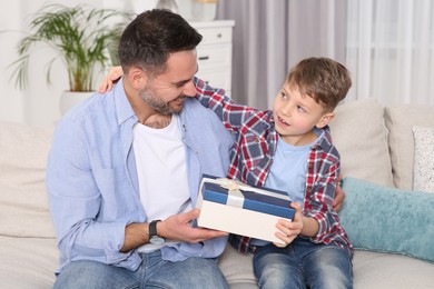 Cute little boy presenting his father with gift on sofa at home