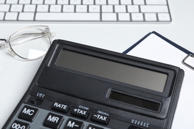 Photo of Calculator, clipboard, keyboard and glasses on white background, closeup. Tax accounting