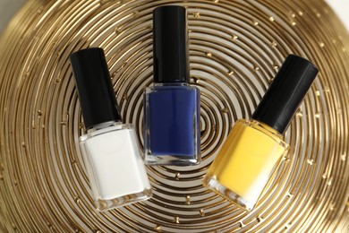 Photo of Stylish presentation of bright nail polishes in bottles on golden textured surface, top view