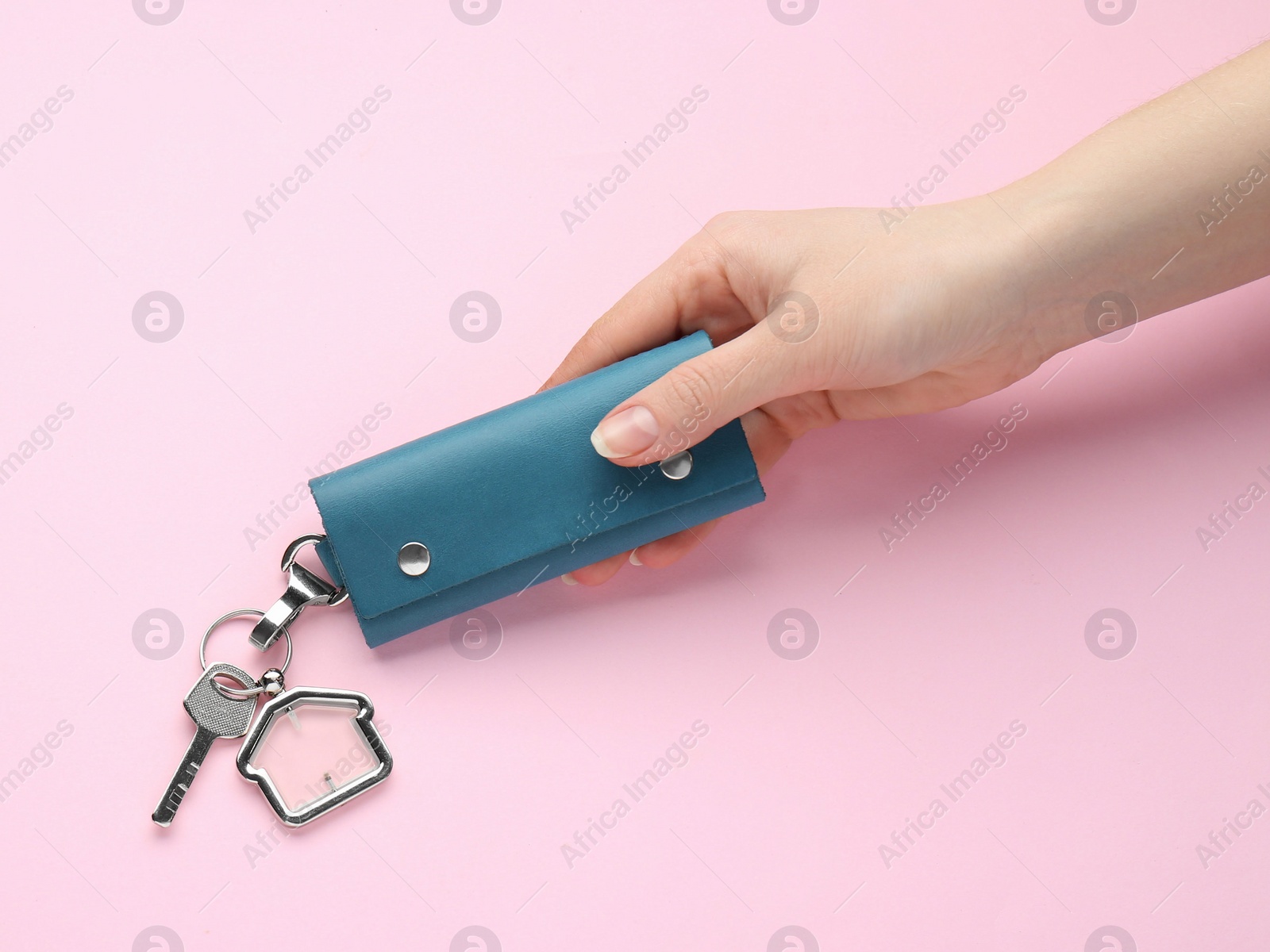 Photo of Woman holding leather case with key on pink background, top view