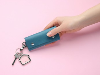 Woman holding leather case with key on pink background, top view