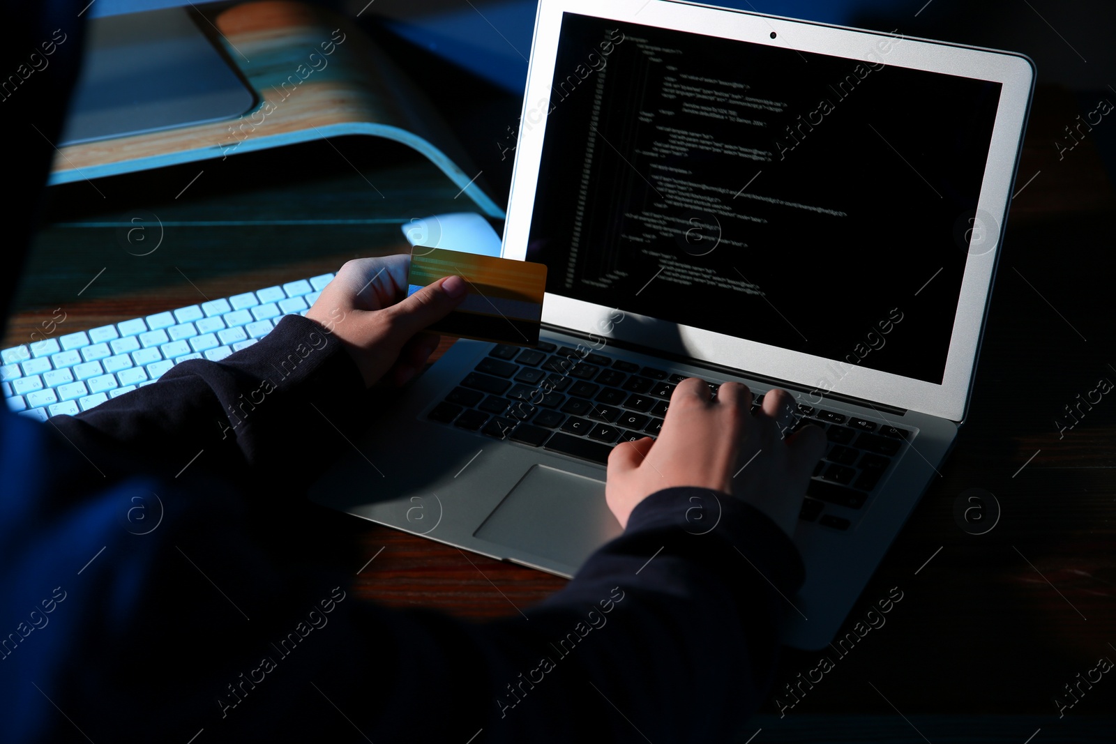 Photo of Hacker with credit card and laptop in dark room, closeup. Cyber crime