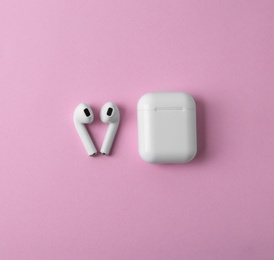 Photo of Modern wireless earphones and charging case on pink background, flat lay. Space for text