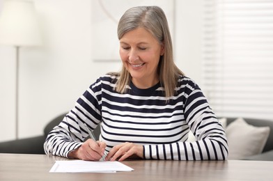 Smiling senior woman signing Last Will and Testament at wooden table indoors