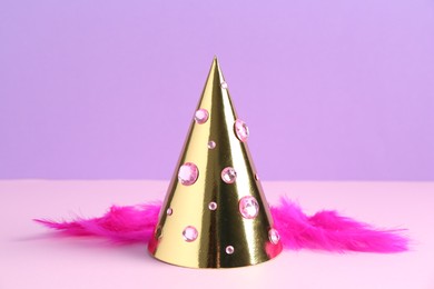 Golden party hat with rhinestones and bright feathers on color background