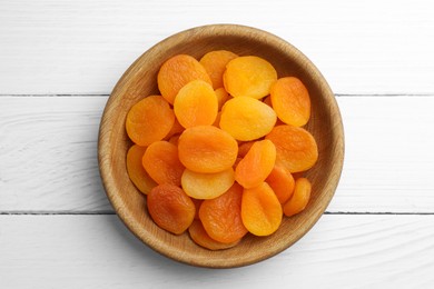 Photo of Bowl of tasty apricots on white wooden table, top view. Dried fruits