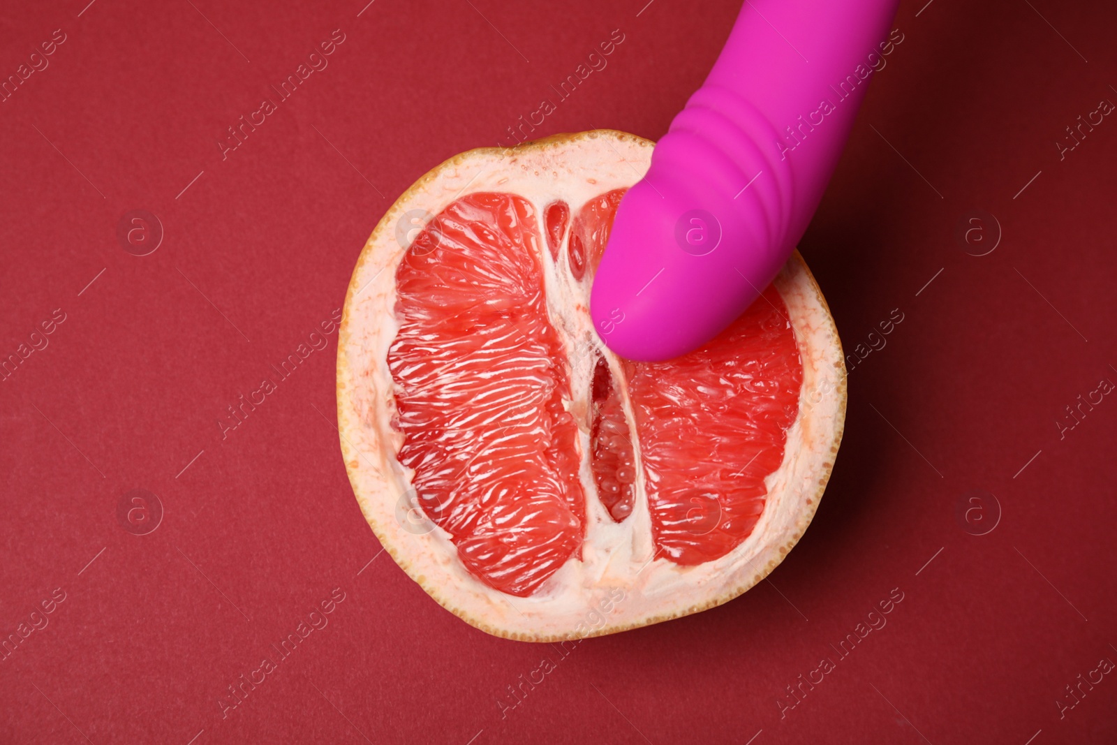 Photo of Half of grapefruit and purple vibrator on red background, flat lay. Sex concept