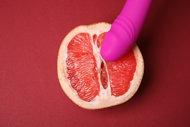 Half of grapefruit and purple vibrator on red background, flat lay. Sex concept