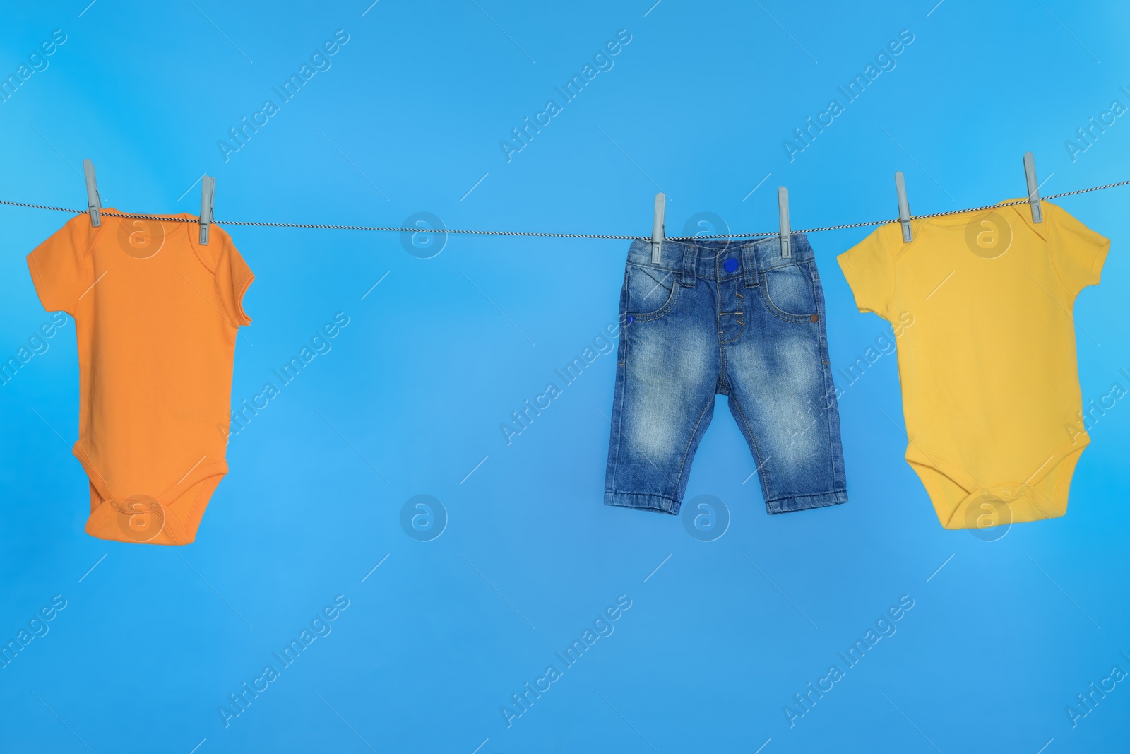 Photo of Different baby clothes drying on laundry line against light blue background