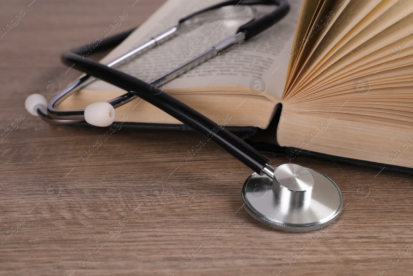 Photo of Open student textbook and stethoscope on wooden table, closeup. Medical education