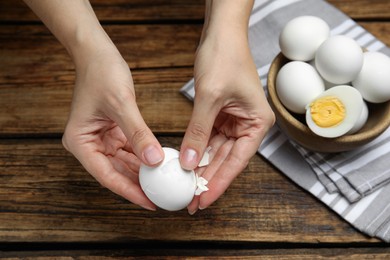 Photo of Woman peeling boiled egg at wooden table, above view