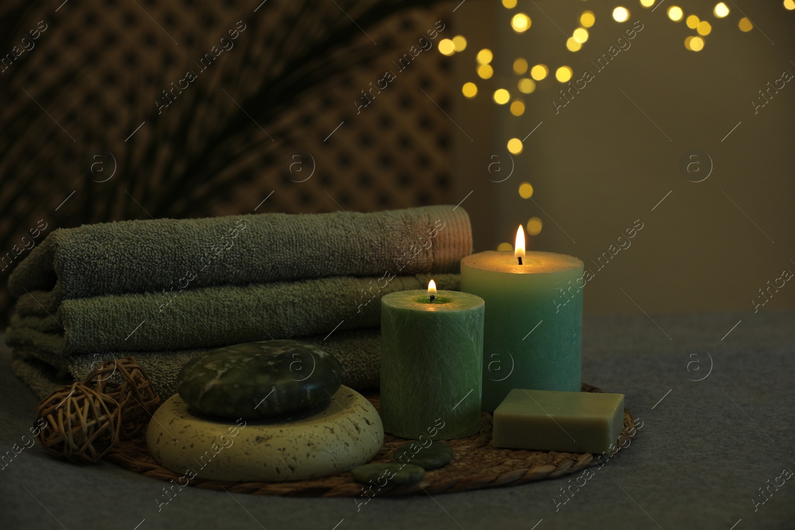 Photo of Spa composition. Burning candles, stones, soap and towels on grey table