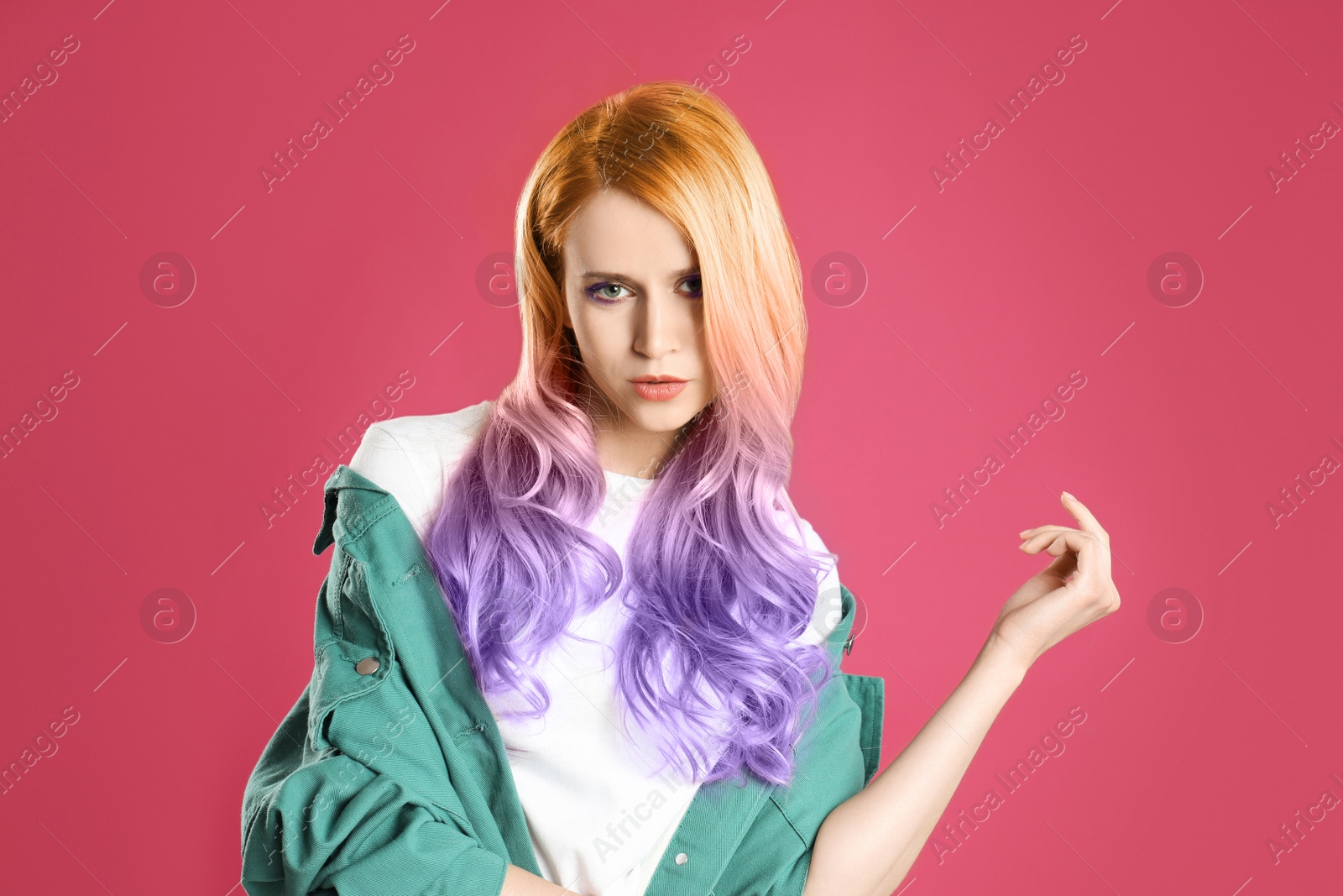 Image of Portrait of young woman with dyed long curly hair on pink background