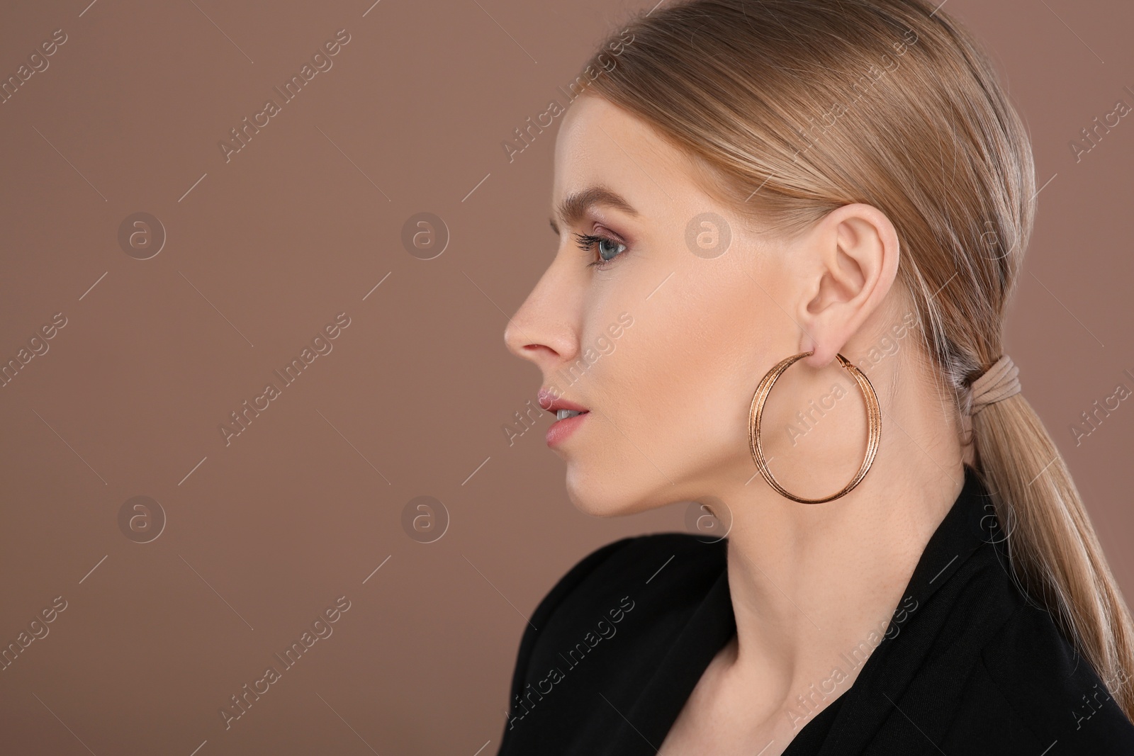 Photo of Beautiful young woman with elegant earrings on light brown background, space for text