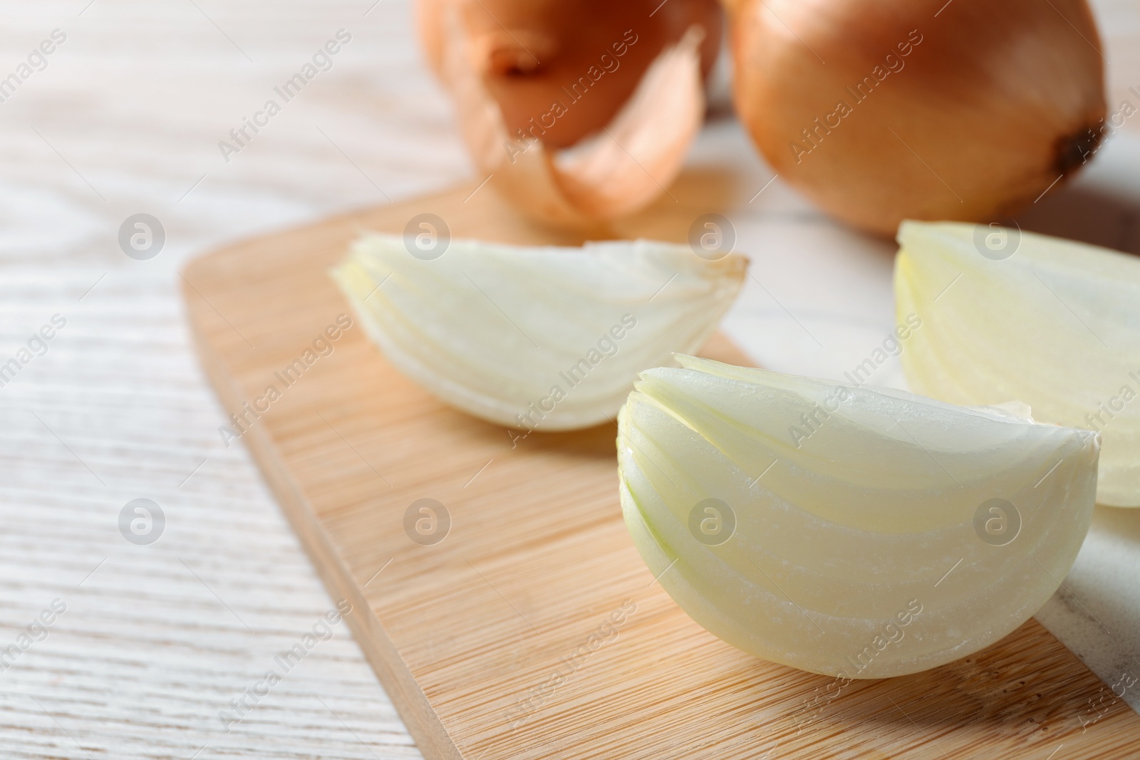 Photo of Whole and cut onions on white wooden table, closeup. Space for text