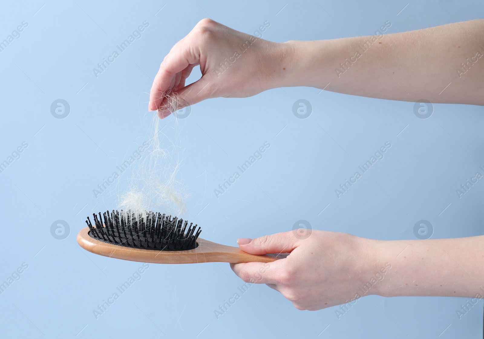 Photo of Woman taking her lost hair from brush on light blue background, closeup