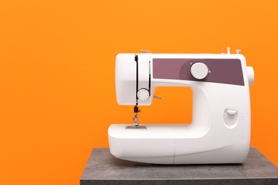 Modern sewing machine on table against color background