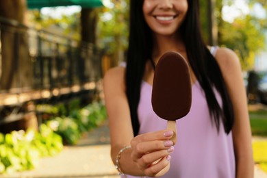 Photo of Young woman holding ice cream glazed in chocolate on city street, closeup. Space for text
