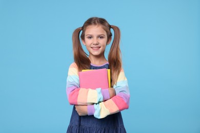 Photo of Happy schoolgirl with books on light blue background