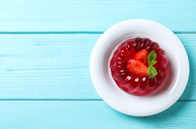 Photo of Delicious red jelly with strawberry and mint on light blue wooden table, top view. Space for text