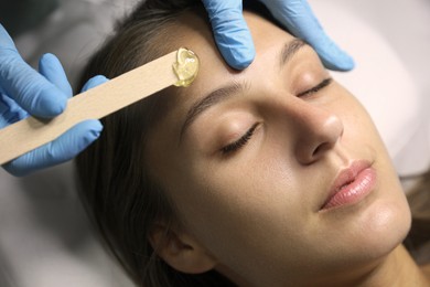 Photo of Young woman undergoing hair removal procedure on face with sugaring paste in salon, closeup