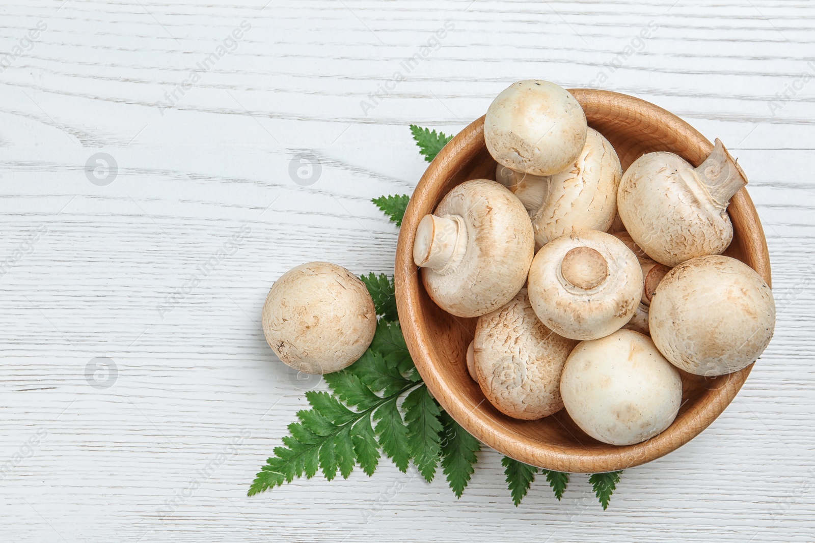 Photo of Bowl of fresh champignon mushrooms on wooden background, top view with space for text