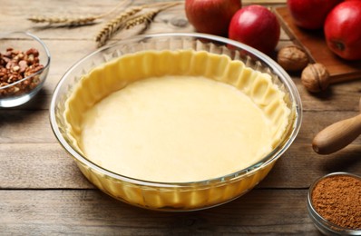 Raw dough and ingredients for apple pie on wooden table