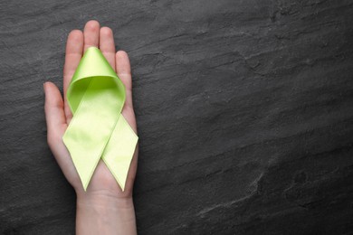 Photo of World Mental Health Day. Woman holding green ribbon on black background, top view with space for text