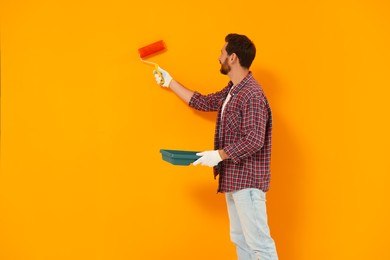 Photo of Designer painting orange wall with dye roller. Space for text