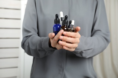 Woman holding bottles with essential oils on blurred background, closeup