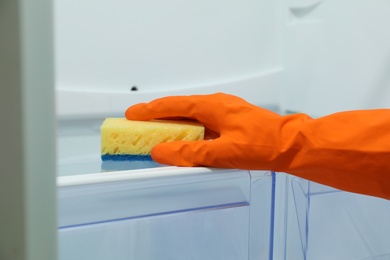 Worker in rubber gloves cleaning empty refrigerator, closeup