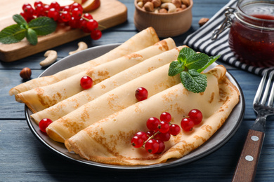 Photo of Delicious thin pancakes with berries on blue wooden table