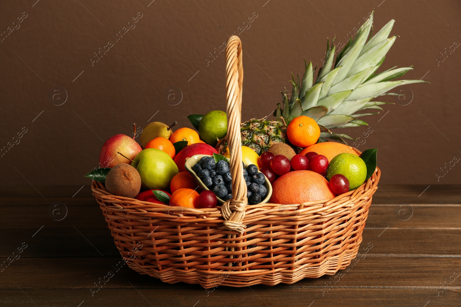 Photo of Assortment of fresh exotic fruits in wicker basket on wooden table