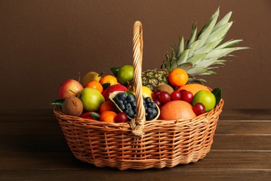 Photo of Assortment of fresh exotic fruits in wicker basket on wooden table
