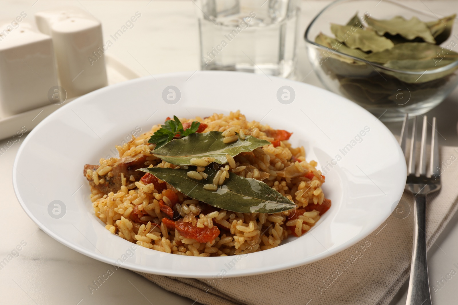 Photo of Delicious pilaf, bay leaves and fork on white table