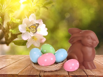 Sweet chocolate bunny and colorful eggs on wooden table outdoors. Easter celebration