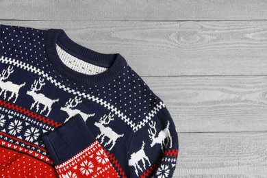 Photo of Warm Christmas sweater on grey wooden table, top view. Space for text