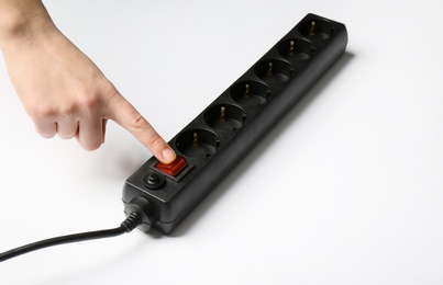 Photo of Woman pressing power button of extension cord on white background, closeup. Electrician's equipment