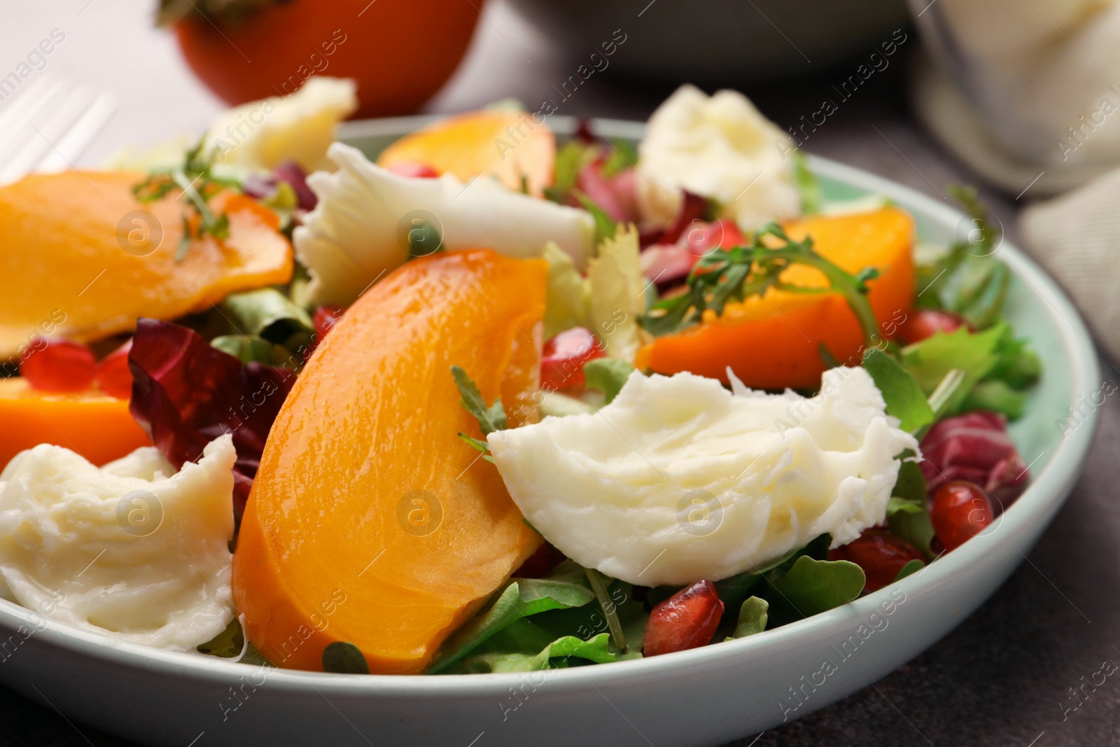 Photo of Delicious persimmon salad with cheese and pomegranate on grey table, closeup